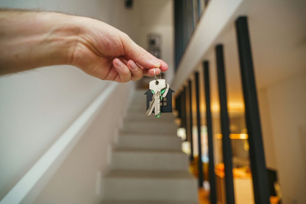 Hand holding new house keys with staircase in the background representing a newly purchased home.